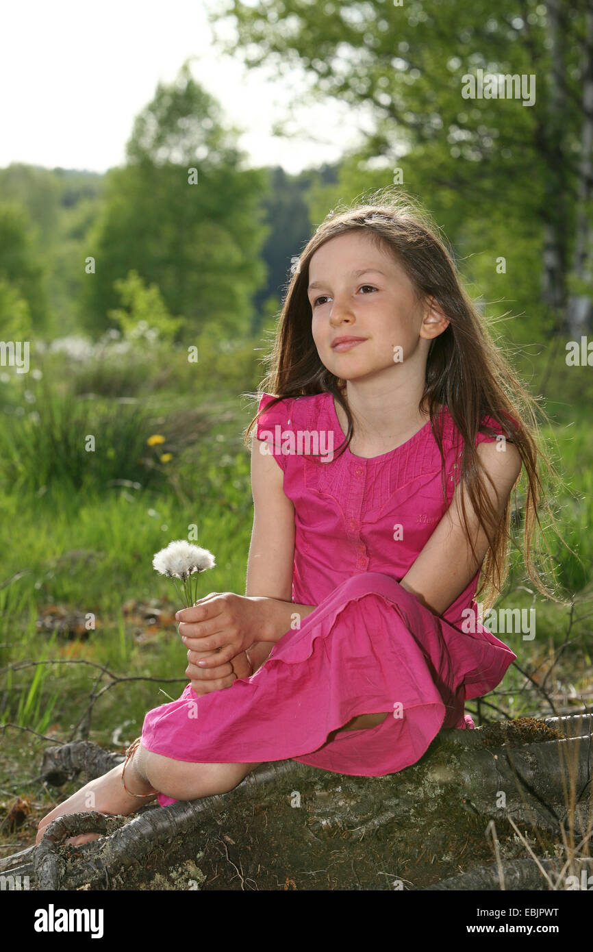 kleines Mädchen sitzt verträumt auf einer Baumwurzel Stockfoto