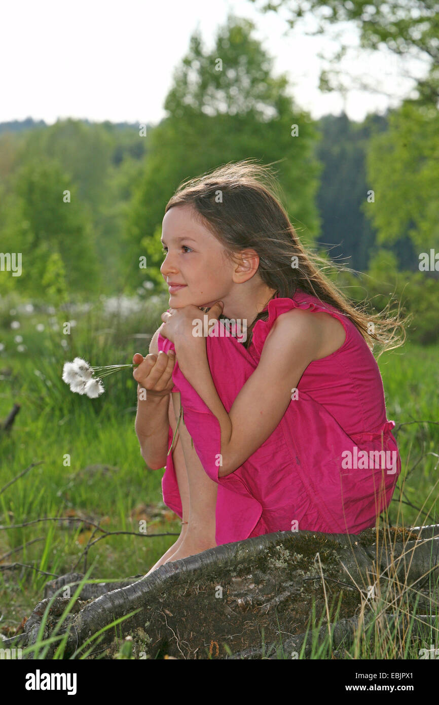 kleines Mädchen sitzt verträumt auf einer Baumwurzel Stockfoto