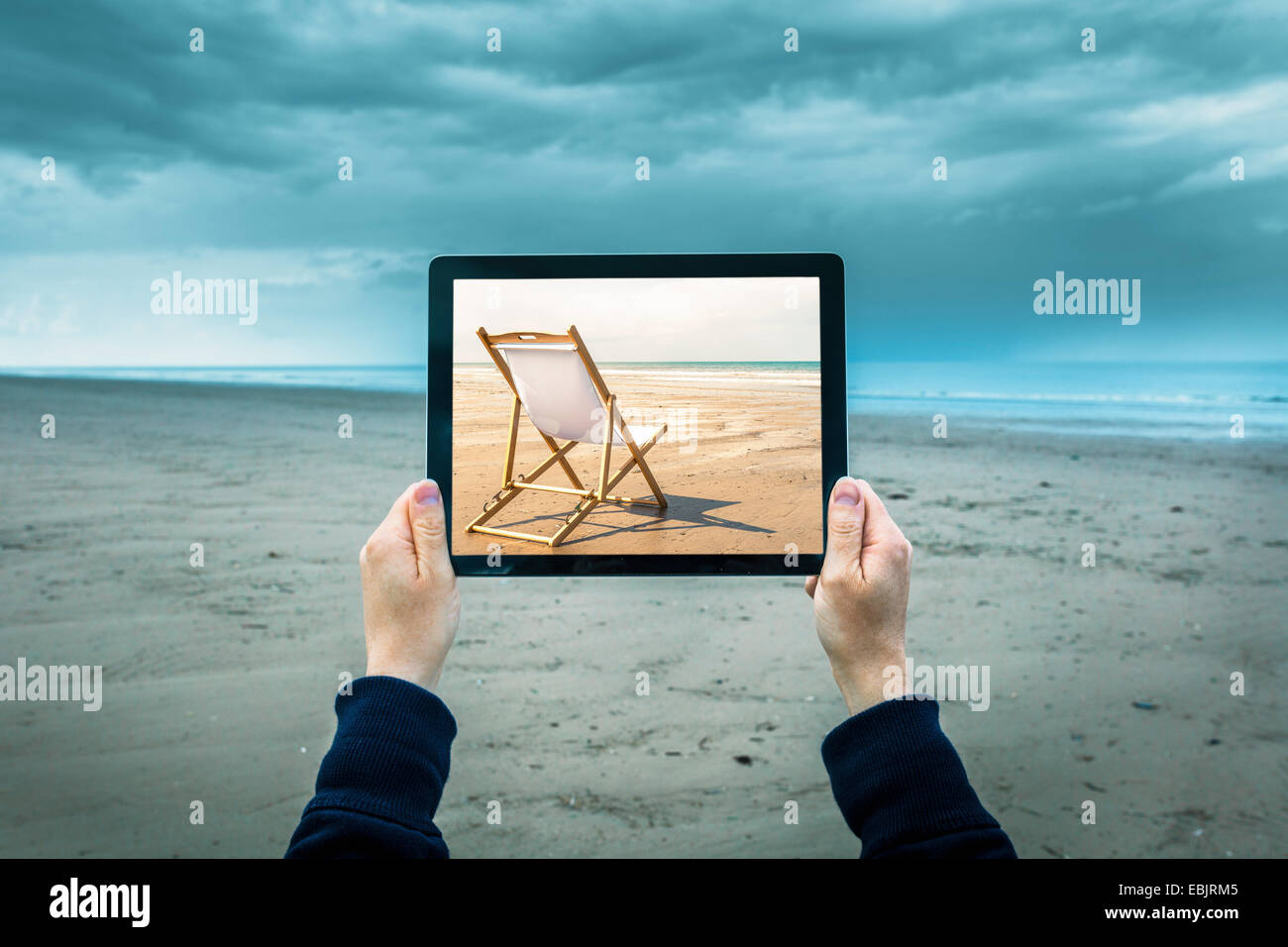 Reife Frau am bewölkten Strand hält digitale Tablet zeigt Sonnenstrand Szene, Fokus auf Hände und laptop Stockfoto