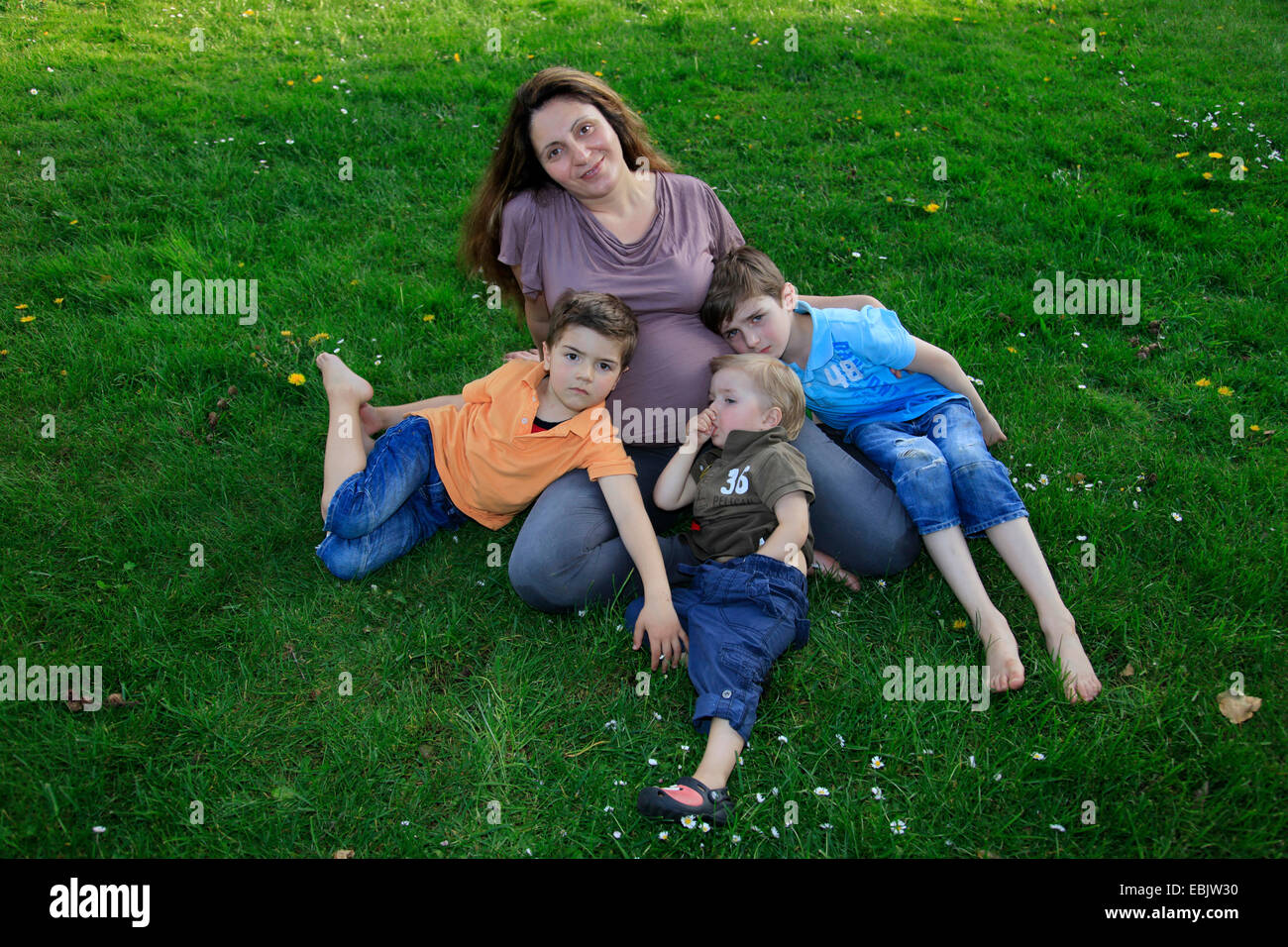 Schwangere Frau liegend auf Wiese mit ihren drei Söhnen Stockfoto