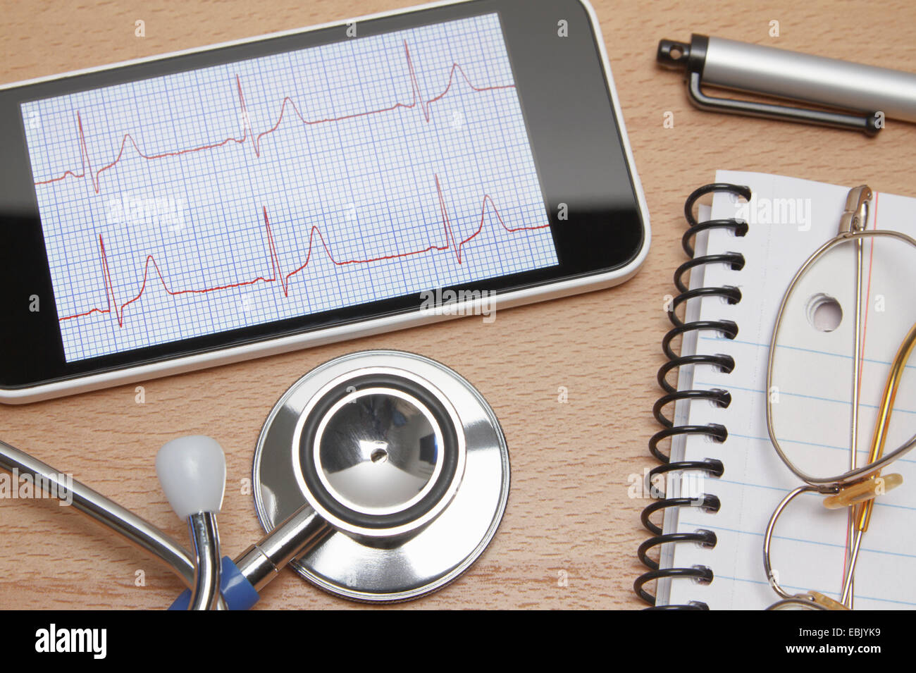 Technologie-Einsatz im Gesundheitswesen. Smartphone zeigt ein Elektrokardiogramm, akustische Stethoskop, Notizblock, Schauspiele und Stift auf Ärzte Büroschreibtisch Stockfoto