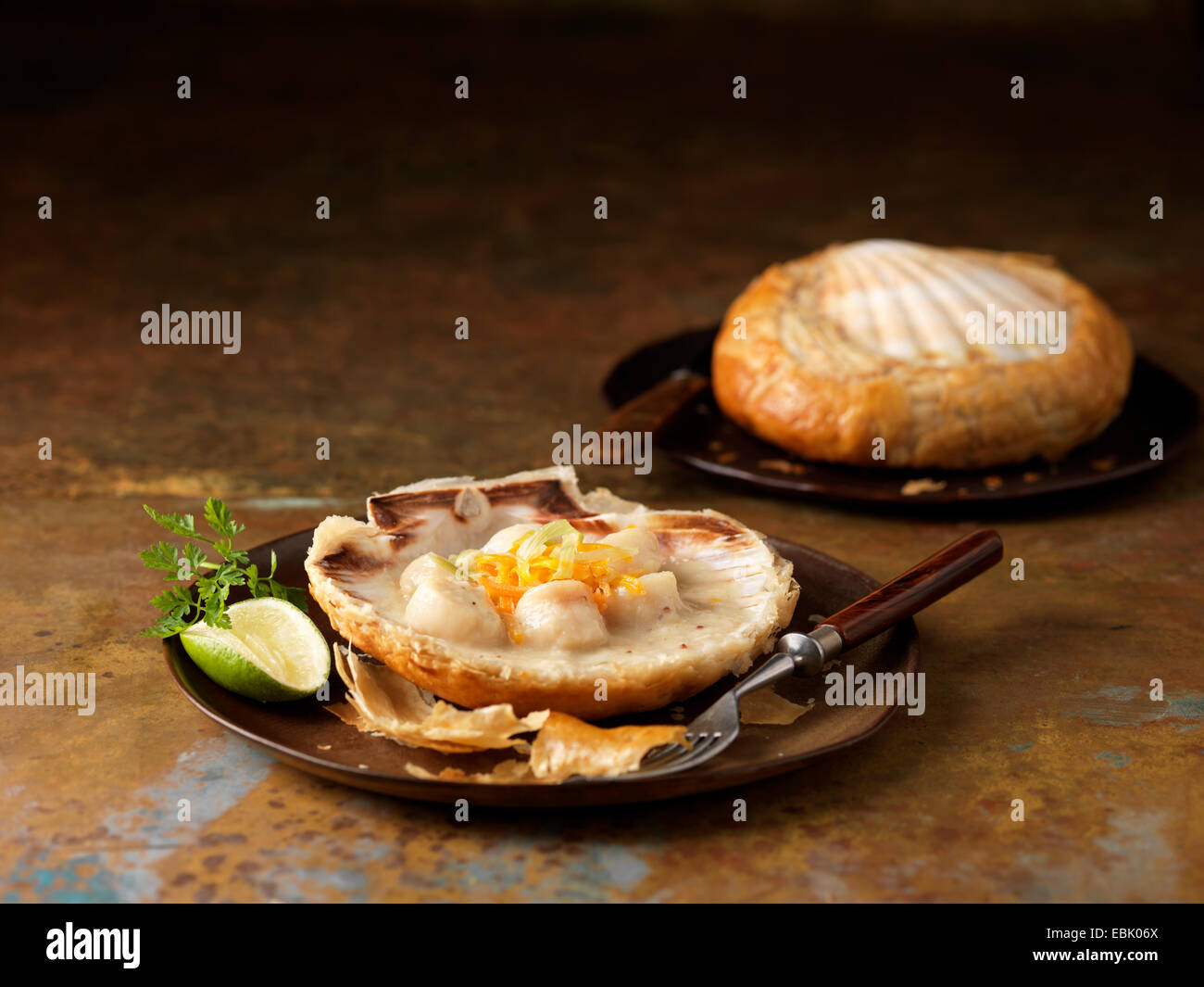 Zwei Jakobsmuscheln gebacken in Schalen mit Wermut, Kerbel garnieren und Limette Stockfoto