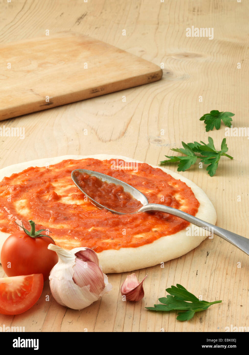 Vorbereiteten Pizzateig bedeckt in Tomatensauce mit Knoblauch und gehackten Tomaten Stockfoto