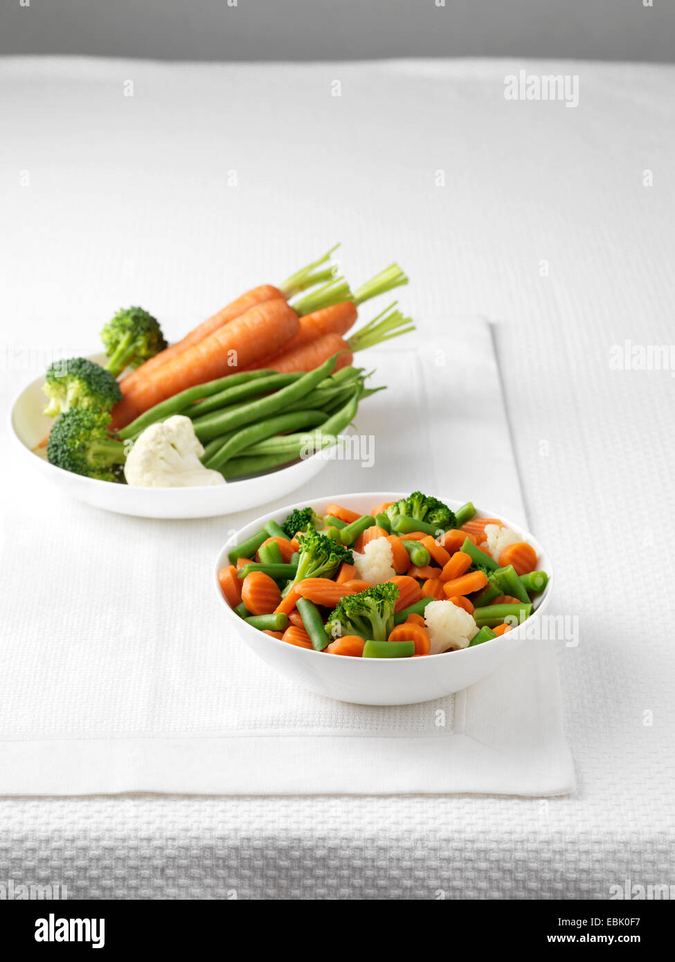 Rohes Gemüse in Schüssel mit Schüssel mit gekochtem Gemüse Stockfoto