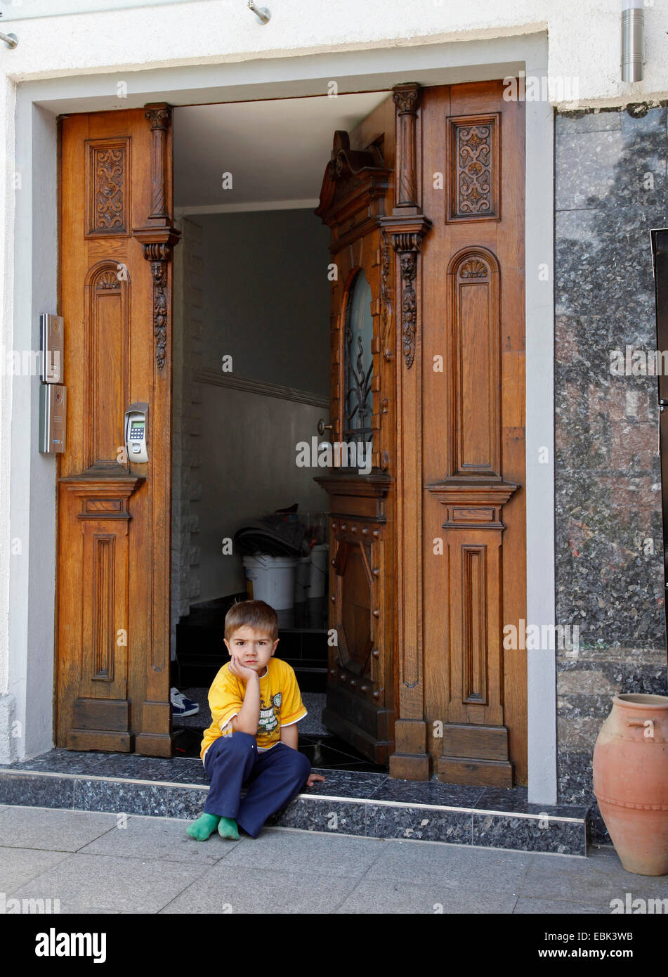 kleiner Junge sitzt vor der geöffneten Eingangstür Stockfoto