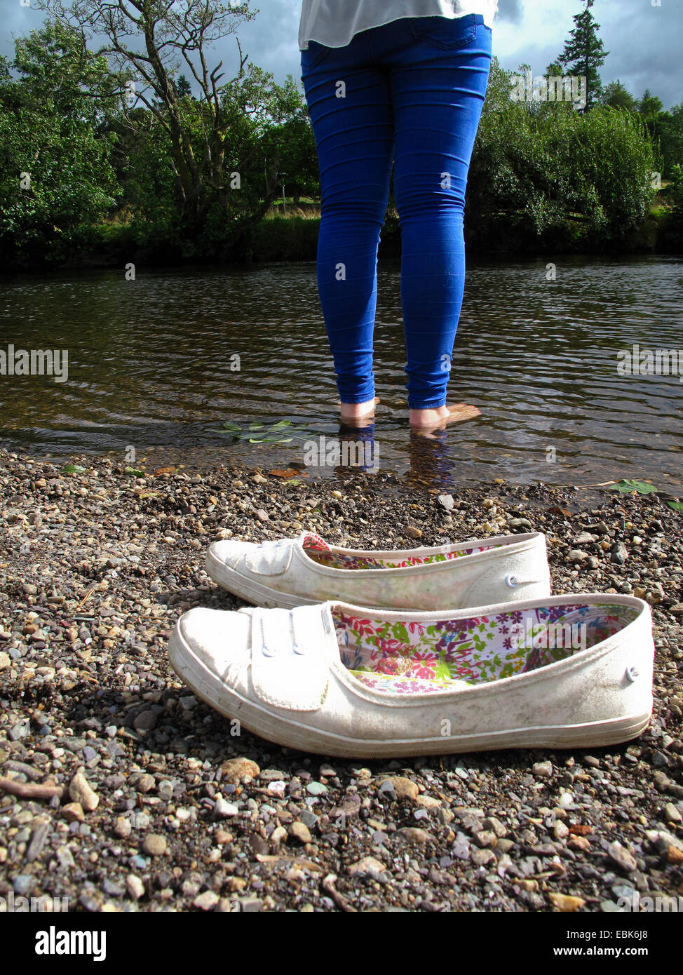 Mädchen im Stream mit Schuhen am Ufer paddeln Stockfoto