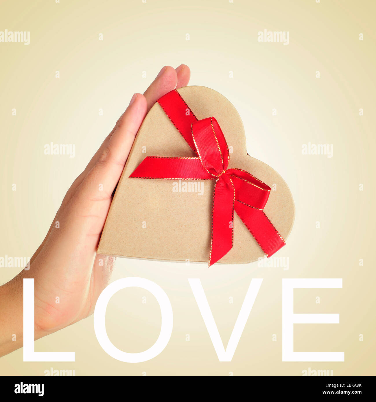 eine herzförmige Geschenkbox mit einer Red ribbon in der Hand eines Mannes und das Wort Liebe in den Vordergrund gebunden Stockfoto