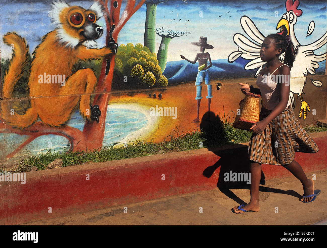 junge Mädchen gehen vor einer bemalten Wand, Madagaskar, Nosy Be, Antsiranana, Hell Ville Stockfoto
