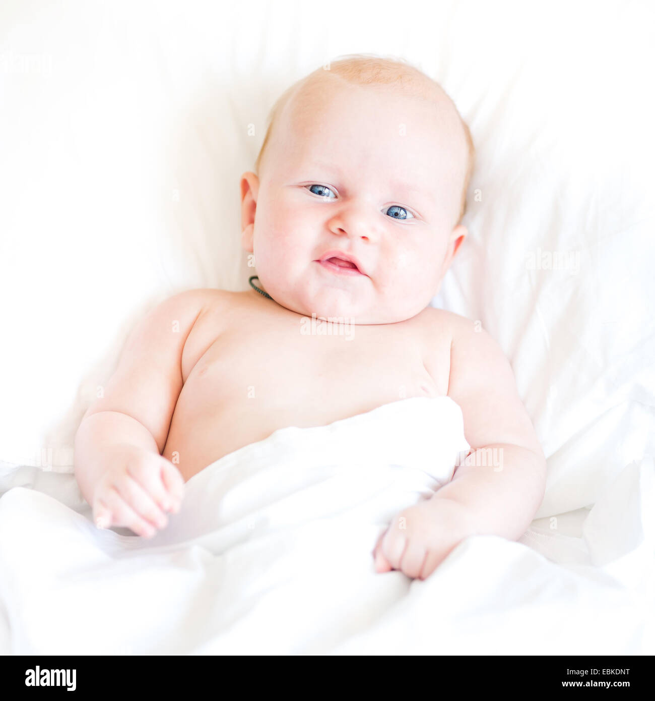 Friedliche neugeborenes Baby liegend auf einem Bett lächelnd auf weißen Laken Stockfoto