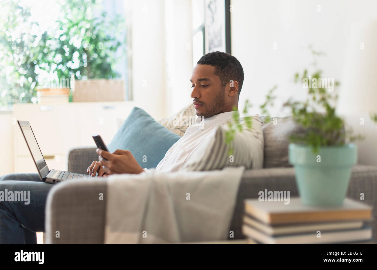 Mann sitzt im Wohnzimmer, mit Laptop und Handy Stockfoto