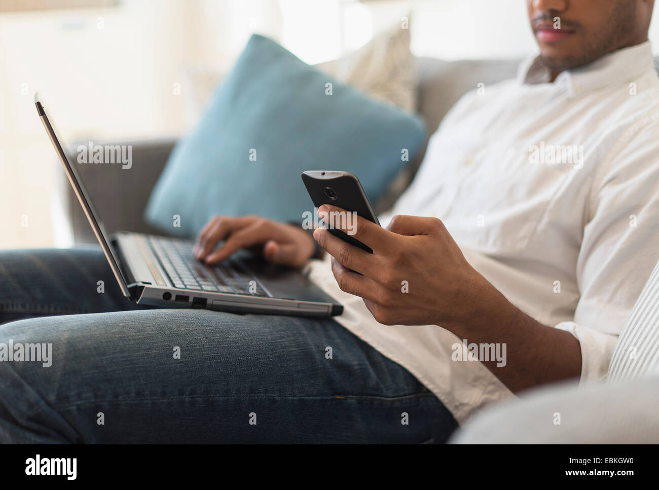 Mann sitzt im Wohnzimmer, mit Laptop und Handy Stockfoto
