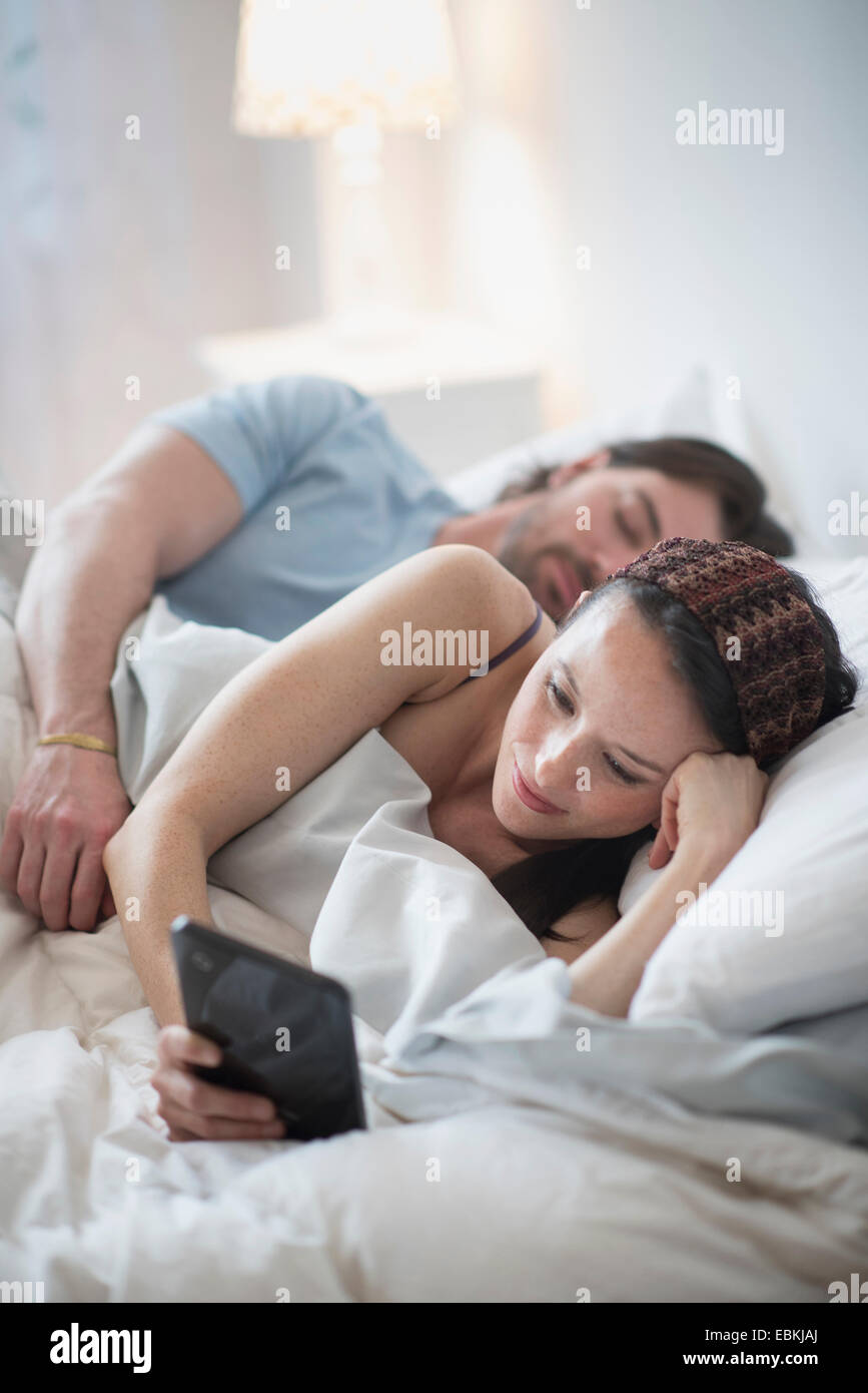 Paar im Bett, Frau liest über digital-Tablette und Man schläft Stockfoto