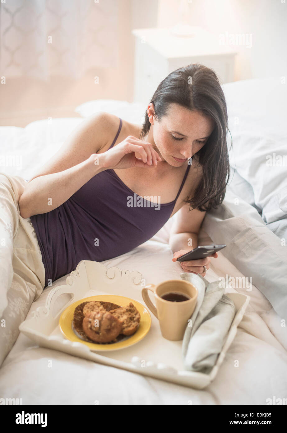 Frau mit Frühstück im Bett, mit Handy Stockfoto