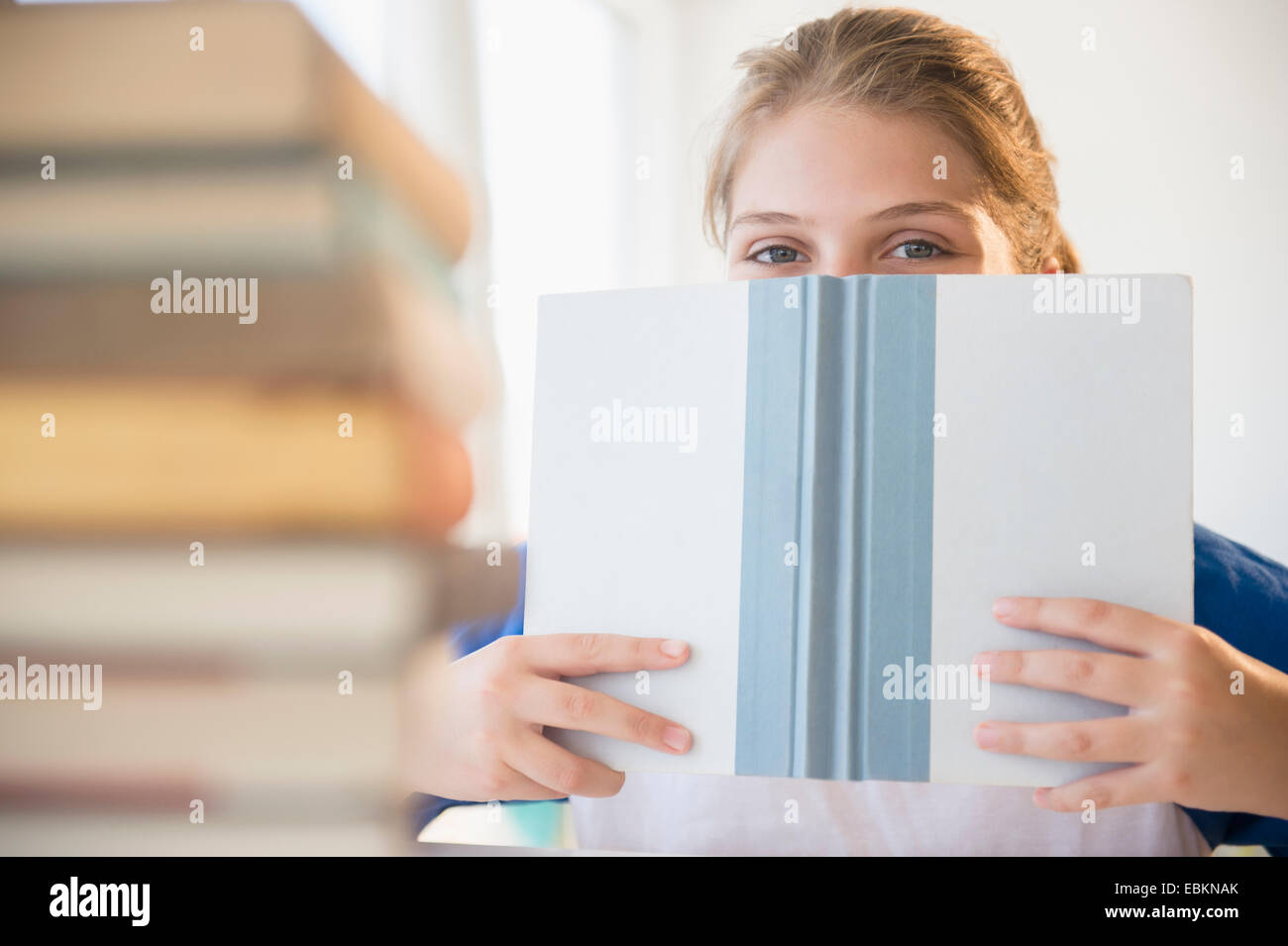 Teenager-Mädchen (12-13) versteckt hinter Buch konfrontiert Stockfoto