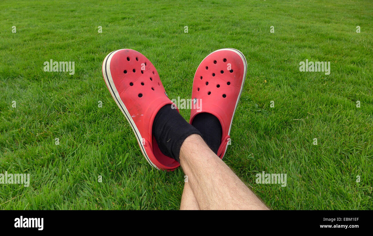 gekreuzten Beinen mit rotem Kautschuk Clogs auf einem grünen Rasen Stockfoto