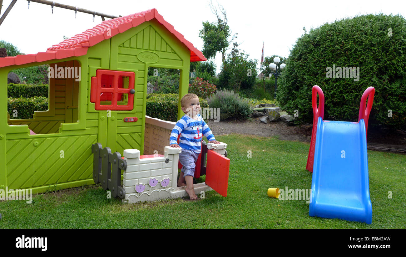 kleiner Junge spielt in einem Garten mit Rutsche und ein Spielhäuschen Stockfoto