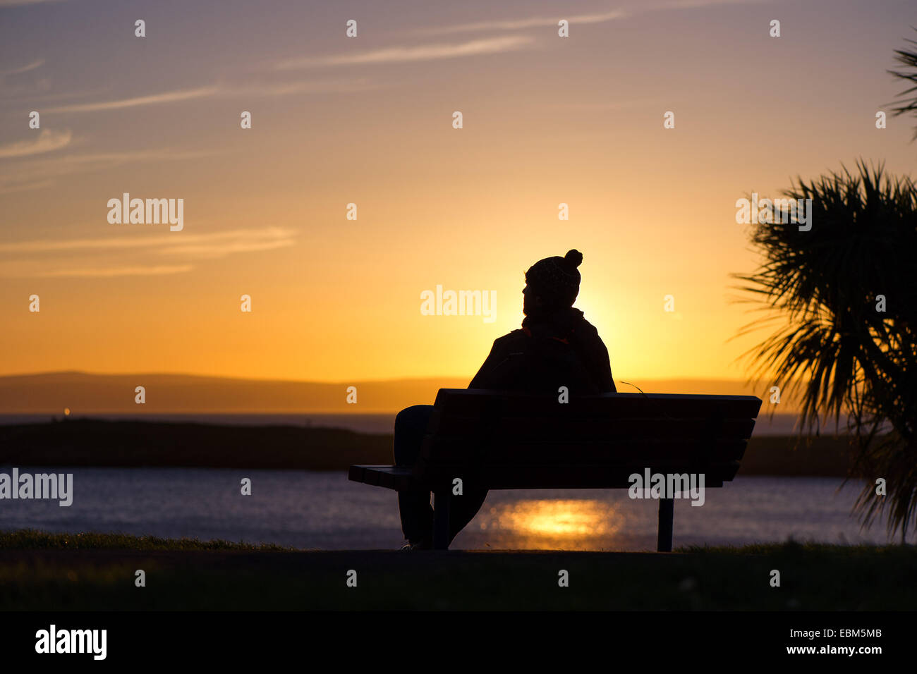 Ein Mann in eine Wollmütze beobachtet den Sonnenuntergang am Strand von Barry Island, Wales. Stockfoto