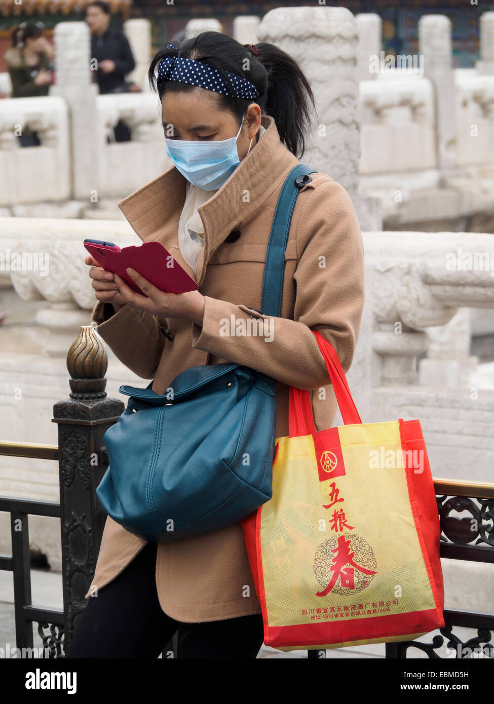 Chinesin verwendet Smartphone, während sie eine Verschmutzungsmaske trägt, weil sie stark raucht - Corona-Coronavirus Corona-Virus Stockfoto