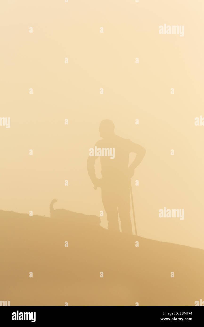 Ein Mann und sein Hund sind durch Nebel Silhouette. Die untergehende Sonne verwandelt sich den Nebel orange. Stockfoto