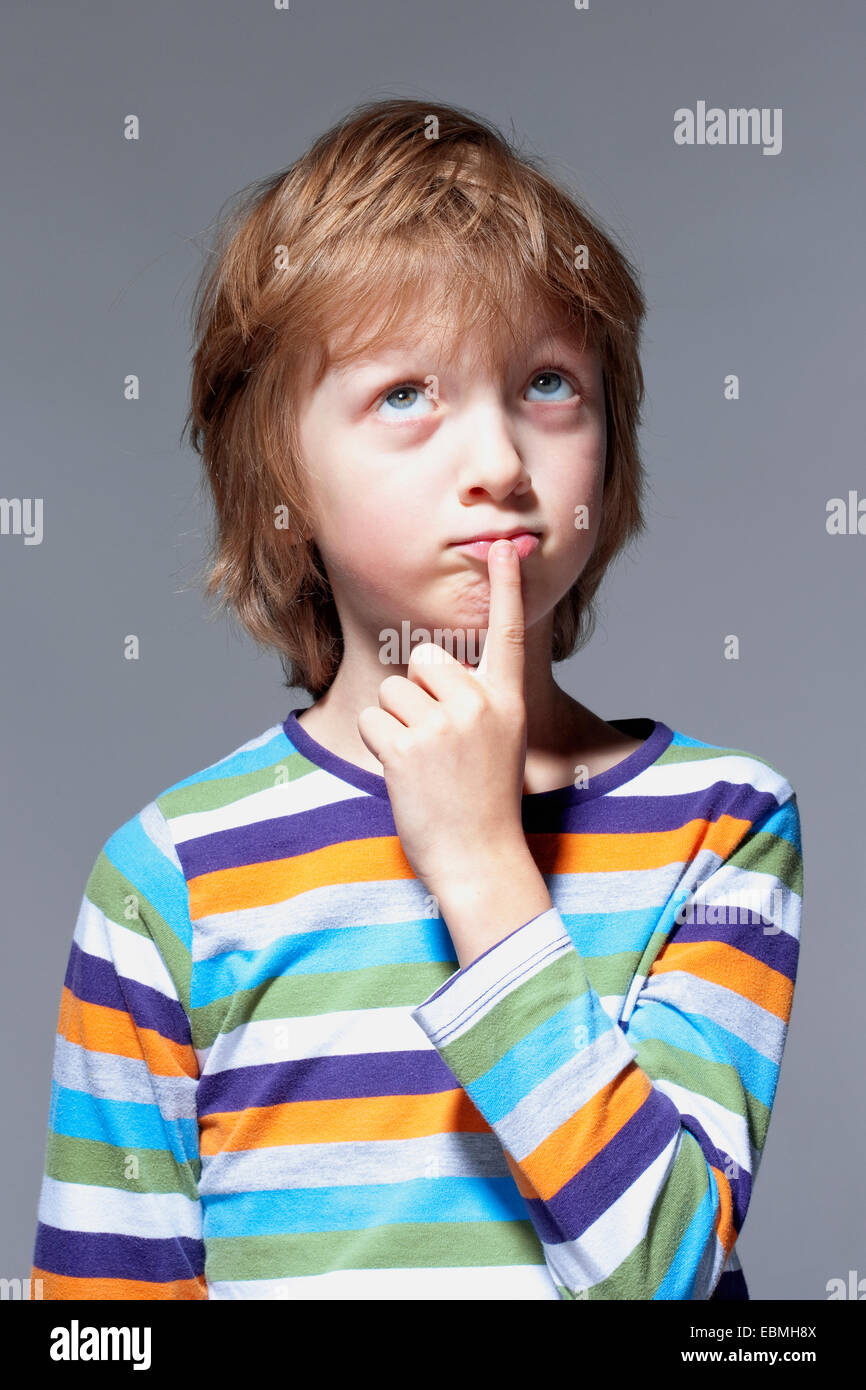 Junge auf der Suche nachdenken, Finger auf den Mund - isoliert auf grau Stockfoto