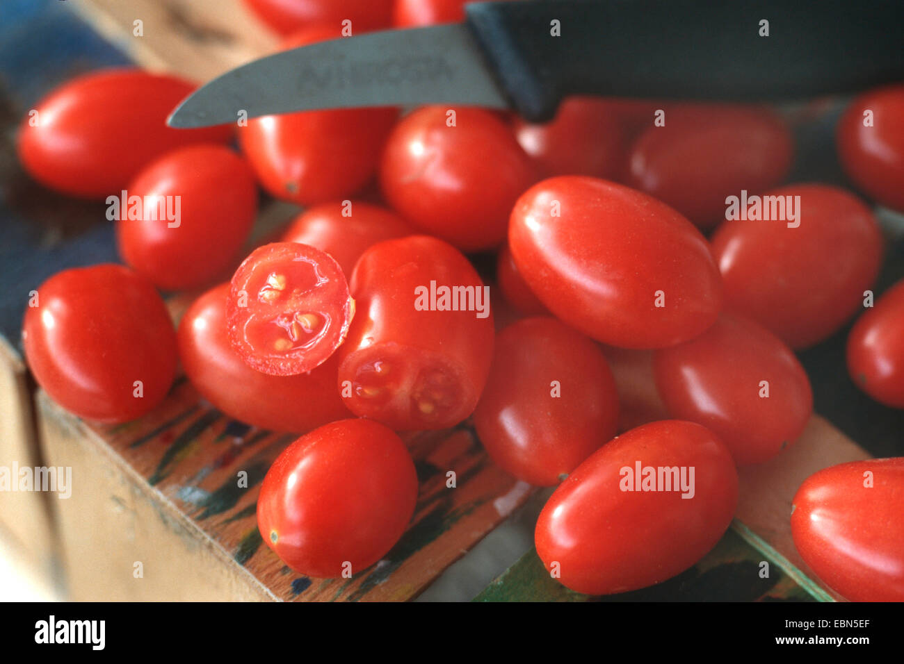 Cherry-Tomate (Lycopersicon Esculentum var. Cerasiforme), Cherry-Tomaten, liegend auf einem Schreibtisch mit einem Küchenmesser Stockfoto