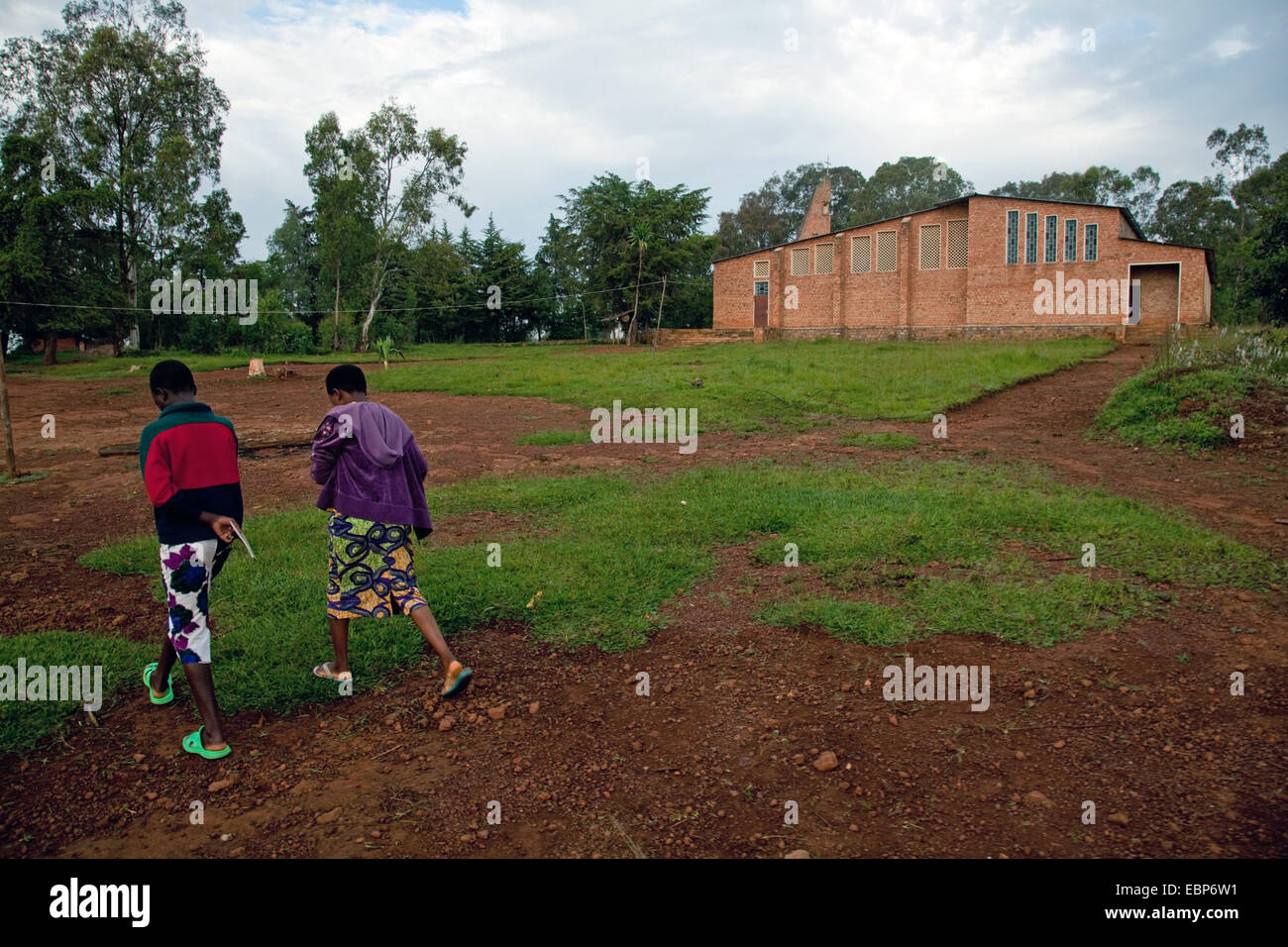 zwei Mädchen, die zu Fuß über einen Platz vor einem bescheidenen Schlamm gemauerte Kirche, Burundi, Cankuzo, in der Nähe von National Parc De La Ruvubu, Cankuzo Stockfoto