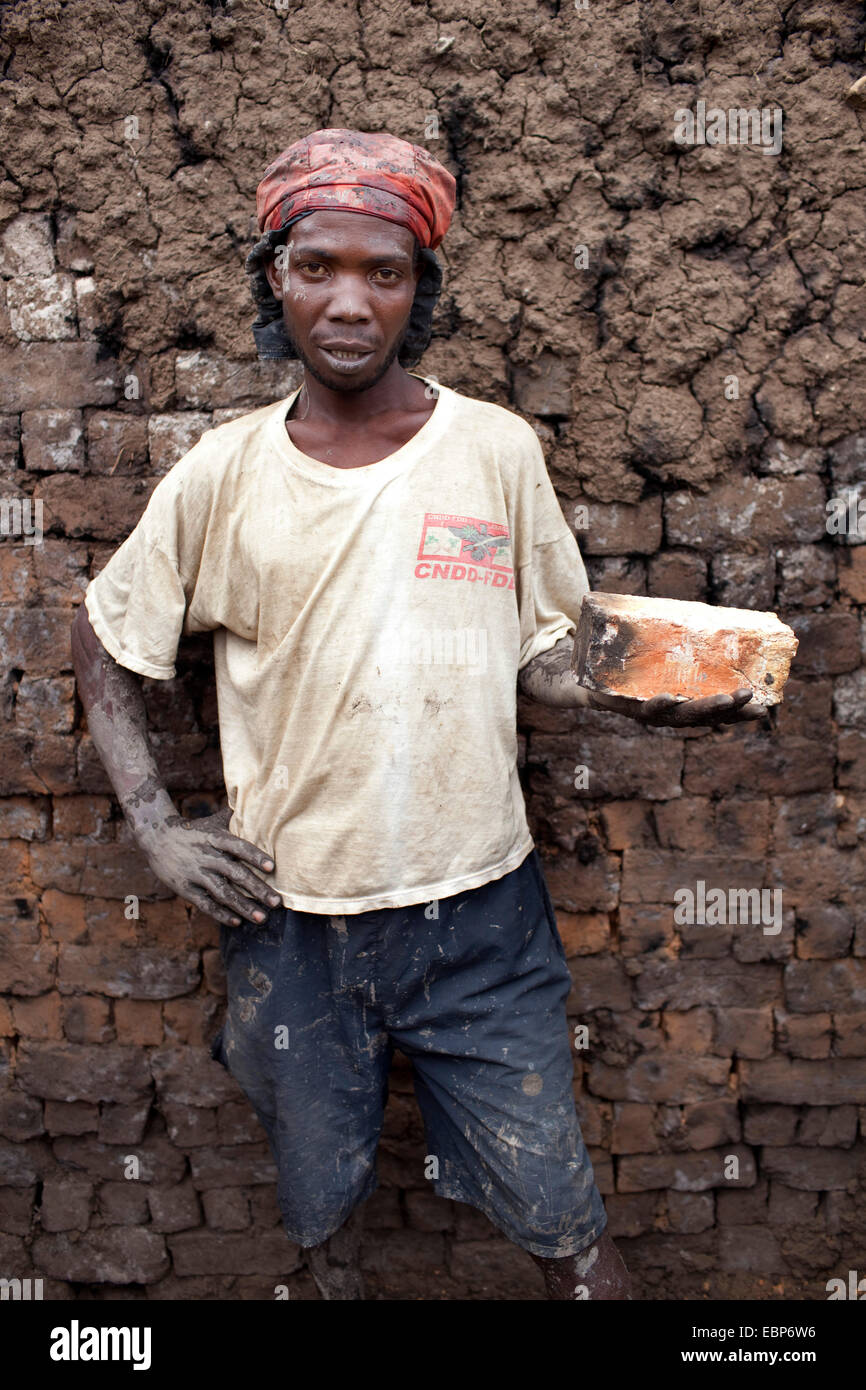 Porträt eines Arbeiters in einer Brickery holding eines der Ziegel in der Hand, die aus Schlamm vor Ort gebildet und in einem traditionellen Ofen verbrannt. Er ist ein T-shirt mit dem Logo der politischen Partei, der aktuelle Präsident, Burundi, Kabezi, Kabezi gewesen. Stockfoto