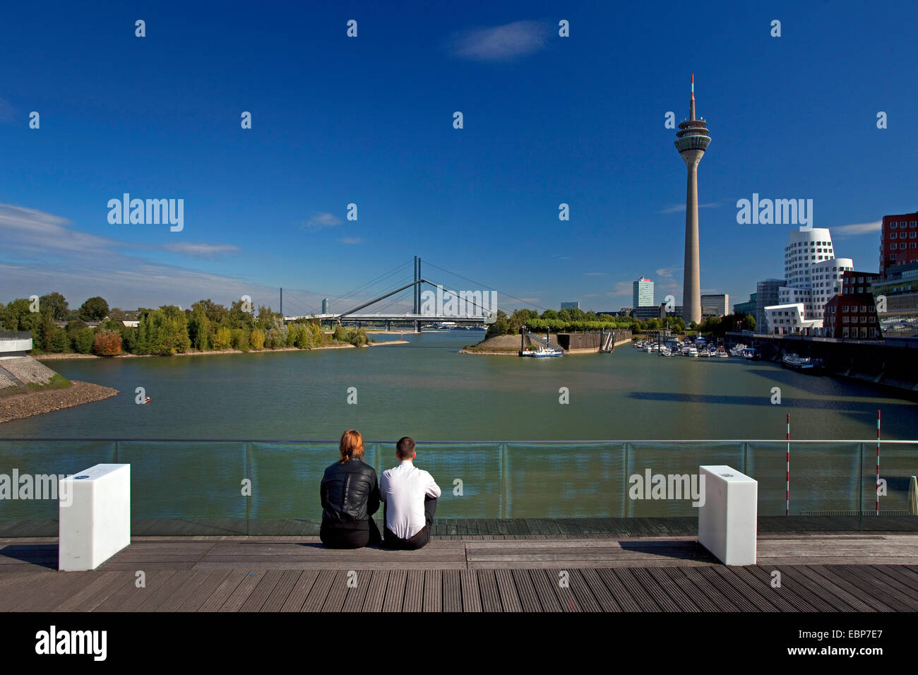 zwei Menschen sitzen am Medien Hafen Düsseldorf, mit Blick auf Rhein, Rheinturm und Rheinkniebruecke, Deutschland, Nordrhein-Westfalen, Düsseldorf Stockfoto