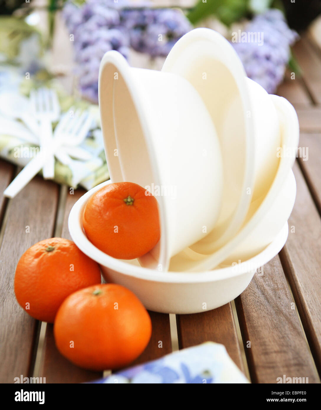 gestapelte Papier Schalen mit Mandarinen auf einem Holztisch mit Blumen im Hintergrund Stockfoto