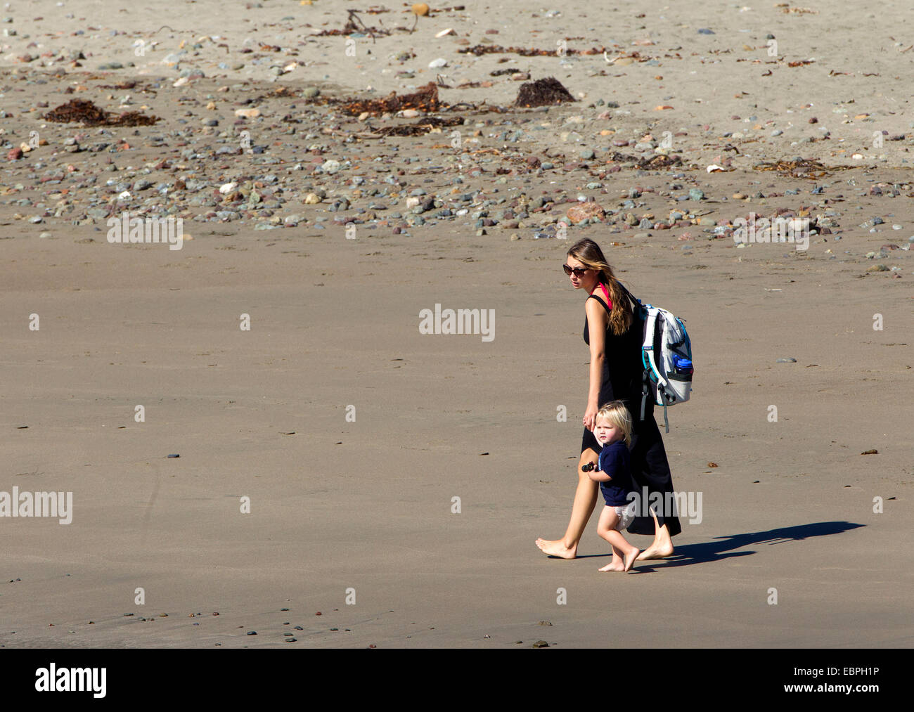 Blondes Kleinkind in Windel zu Fuß entlang der Küste mit Mama Stockfoto