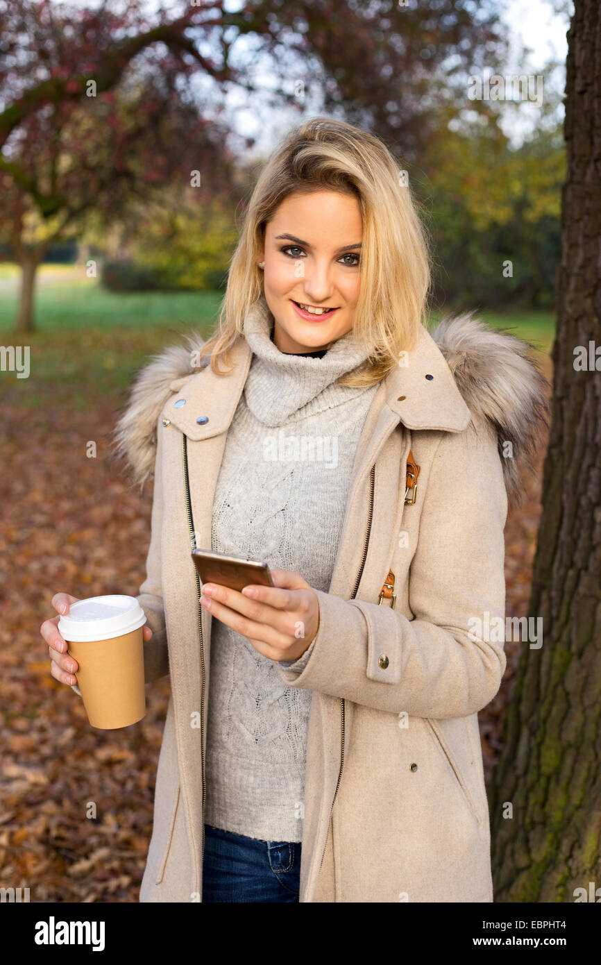 junge Frau liest ihre SMS-Nachrichten mit einem Kaffee im Park. Stockfoto