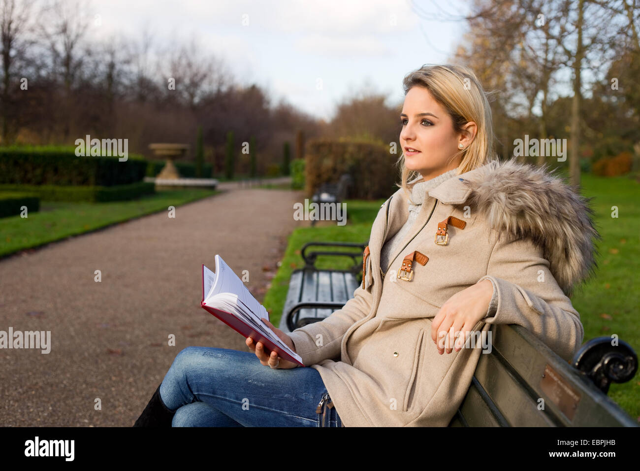 junge Frau hält ihr Tagebuch und sitzt auf einer Parkbank Stockfoto