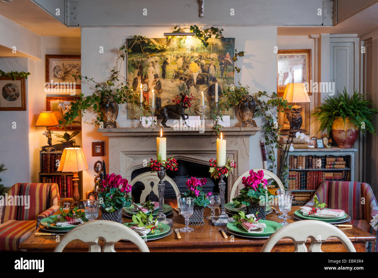 Eine festliche Note hinzufügen ein gedeckter Tisch im Zimmer mit Kelim gepolsterten Sesseln und Kamin, Kerzen und Alpenveilchen. Stockfoto