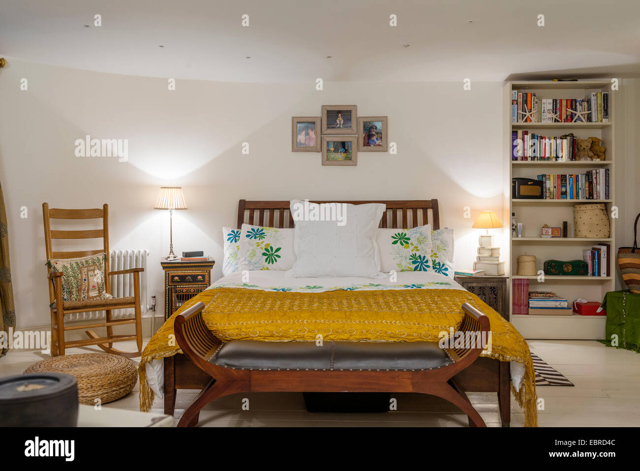 Schaukelstuhl in Schlafzimmer mit gelber Seide Bettdecke und Bücherregal Stockfoto