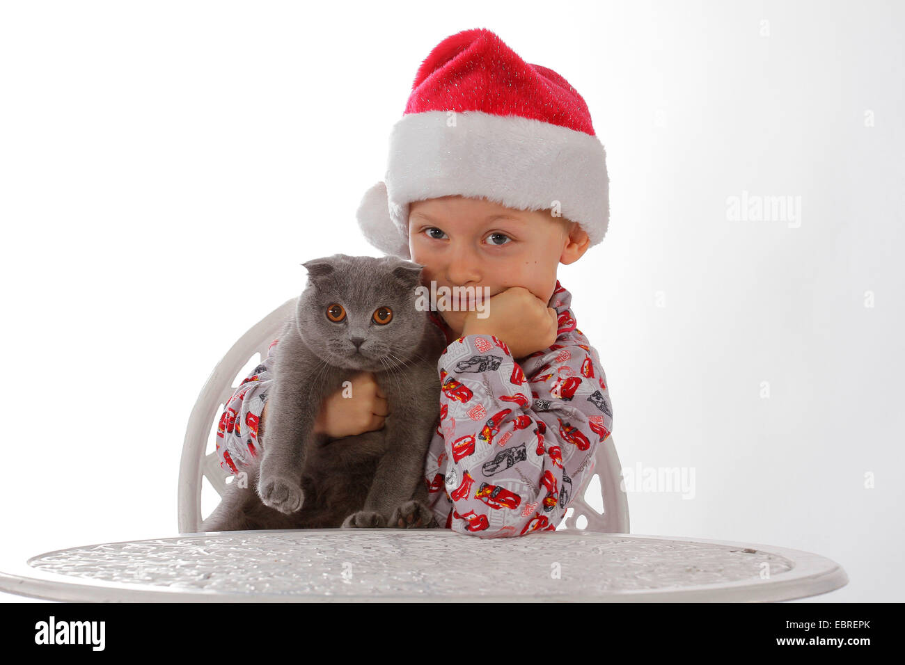 Hauskatze, Hauskatze (Felis silvestris f. catus), Kind mit Santa ┤ s hat an einem Tisch sitzen mit einer Katze im Arm Stockfoto