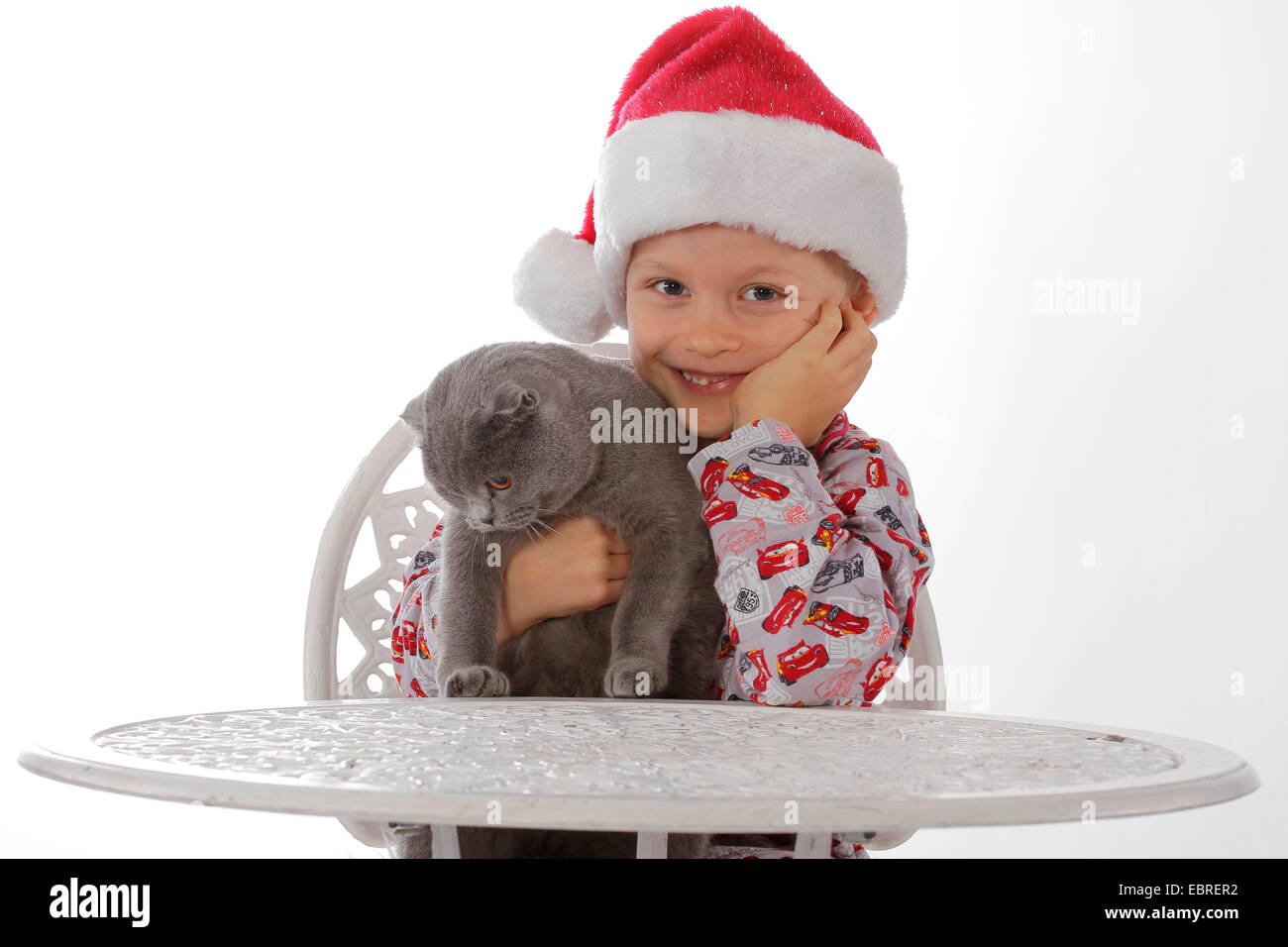 Hauskatze, Hauskatze (Felis silvestris f. catus), Kind mit Santa ┤ s hat an einem Tisch sitzen mit einer Katze im Arm Stockfoto