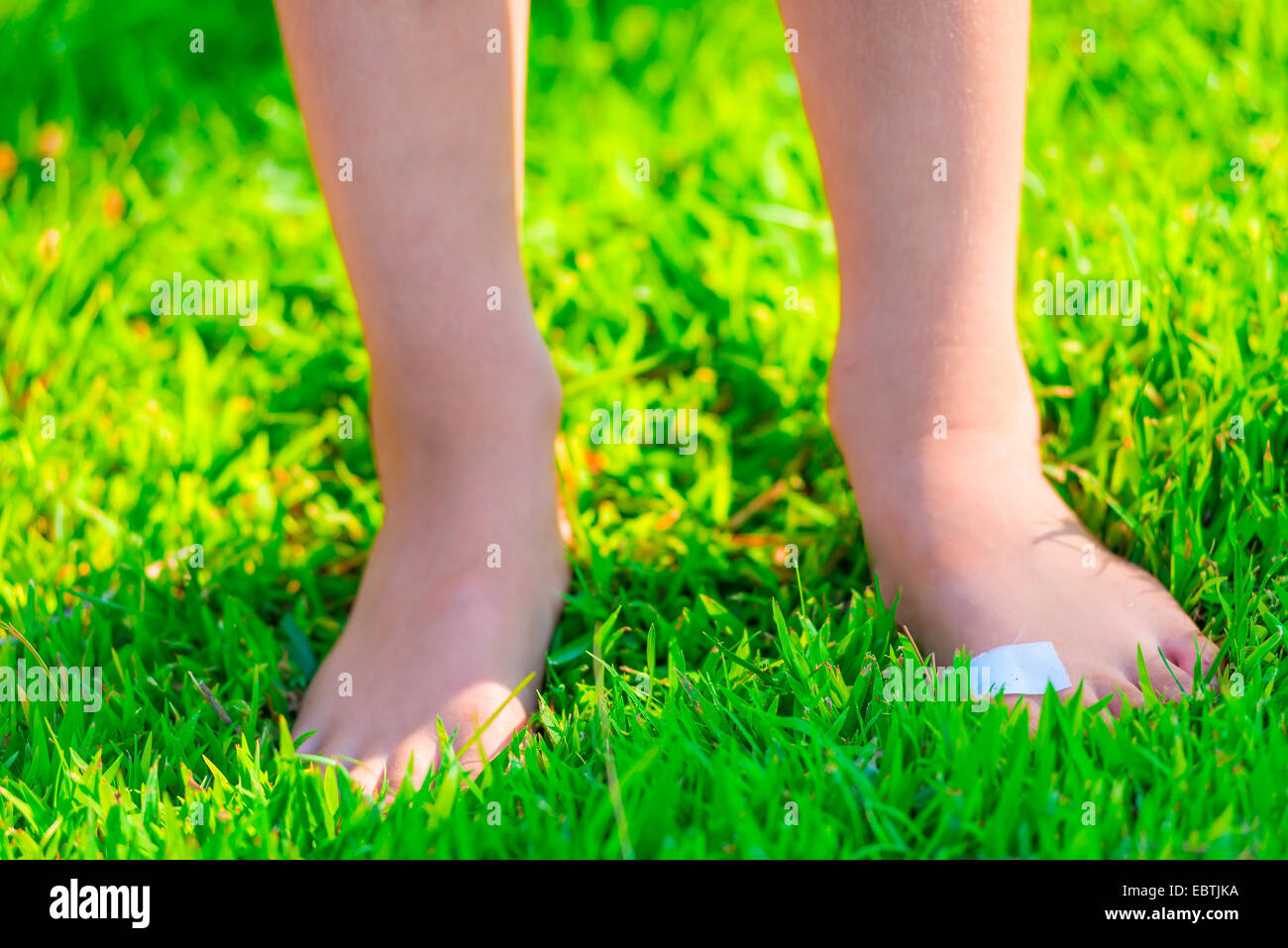barfuß steht Kind mit einem Pflaster auf einem Fuß auf dem grünen Rasen Stockfoto