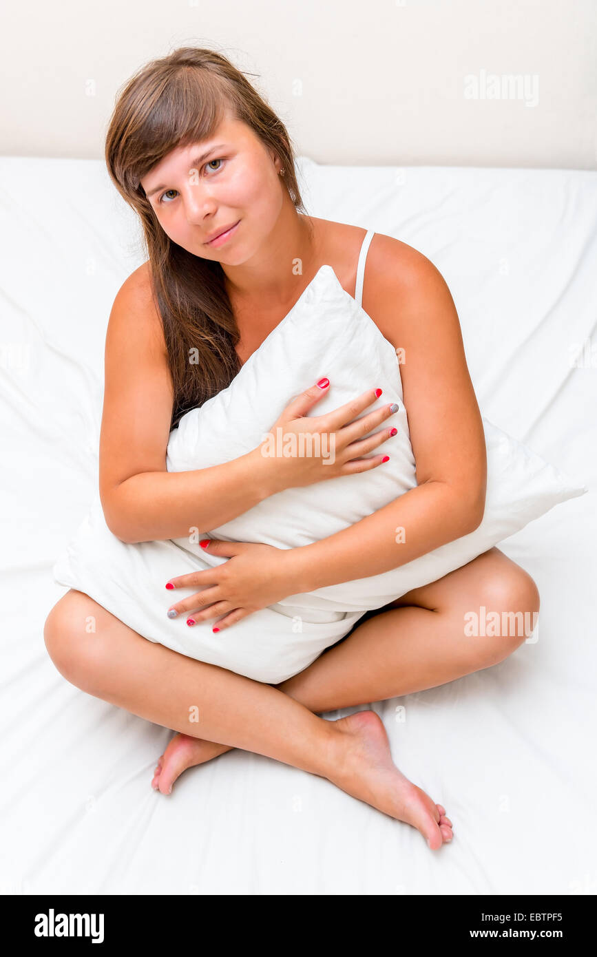 ein charmantes junges Mädchen umarmt eine Kissen im Bett Stockfoto