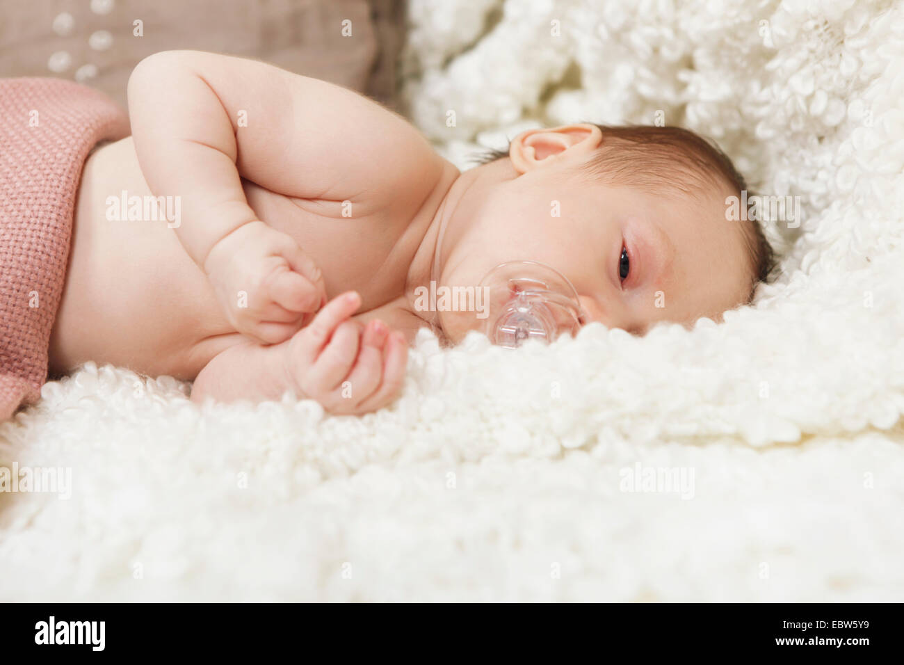 Baby mit Schnuller ist müde im Bett auf einer weißen Decke Stockfoto