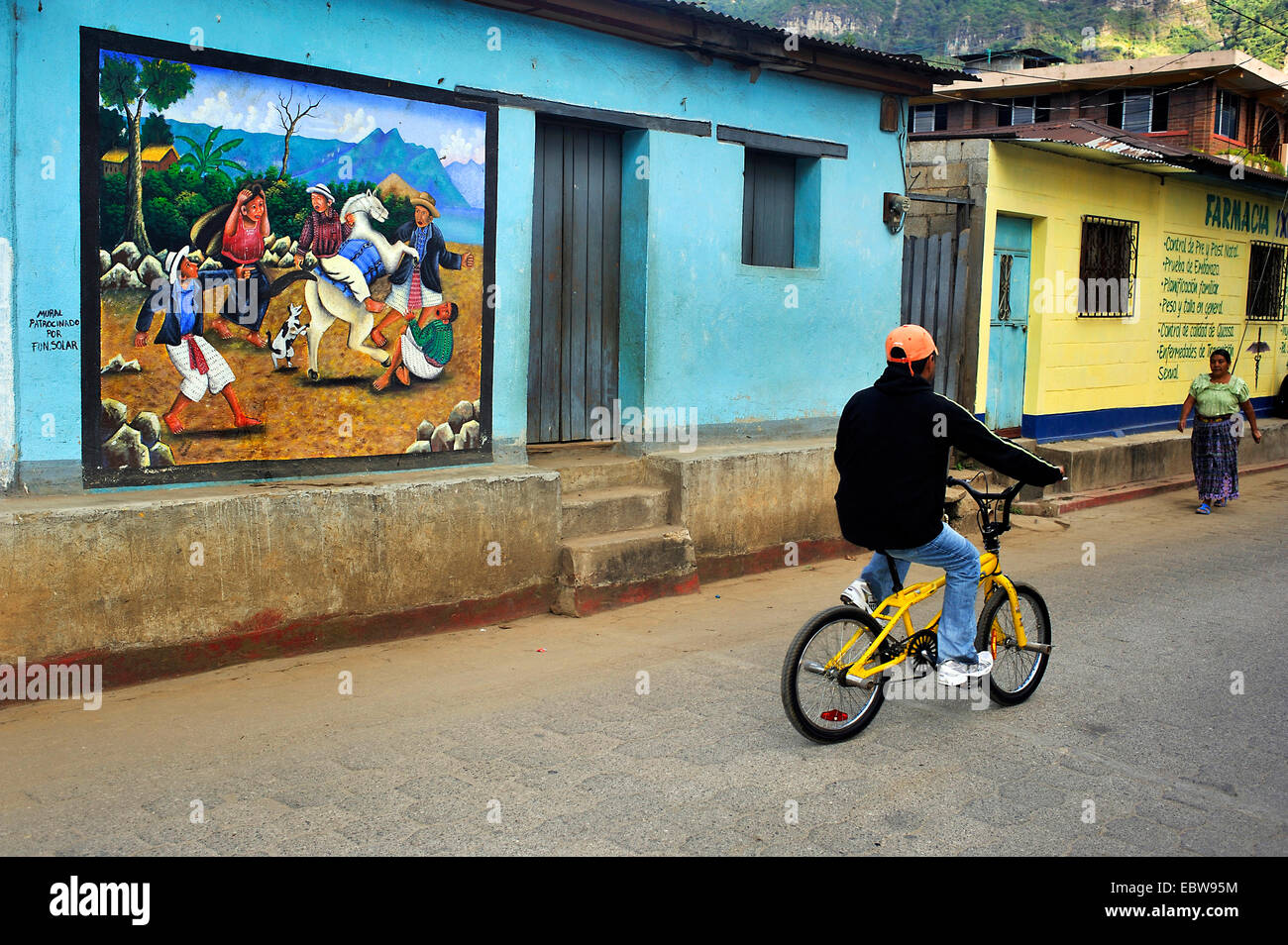 Junge mit dem Fahrrad vorbei an einer auffälligen Wandmalerei bei einer Haus-Fassade, Guatemala, Atitlan See, Santa Cruz la Laguna Stockfoto
