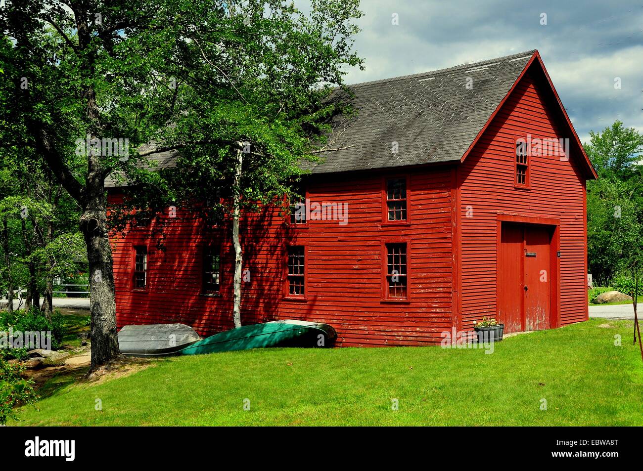 HARRISVILLE, NEW HAMPSHIRE: zwei hölzerne Ruderboote liegen neben eine leuchtend rote Bootshaus im historischen Ortsteil Stockfoto