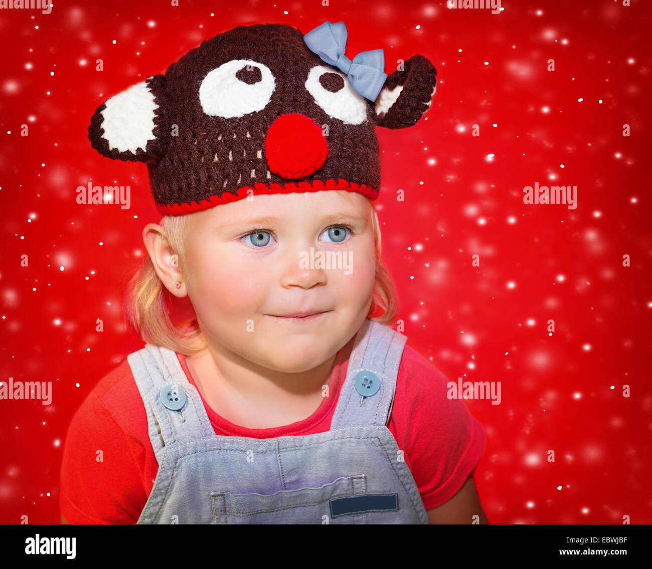 Closeup Portrait ein kleines Baby Mädchen tragen lustige Rudolph Hut über verschneite rotem, Weihnachts-Feier-Konzept Stockfoto