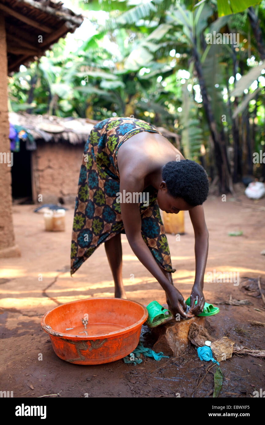 junge Frau in traditioneller afrikanischer Kleidung waschen sich vor ihrem Lehmhaus am Morgen, Burundi, Karuzi, Buhiga Stockfoto