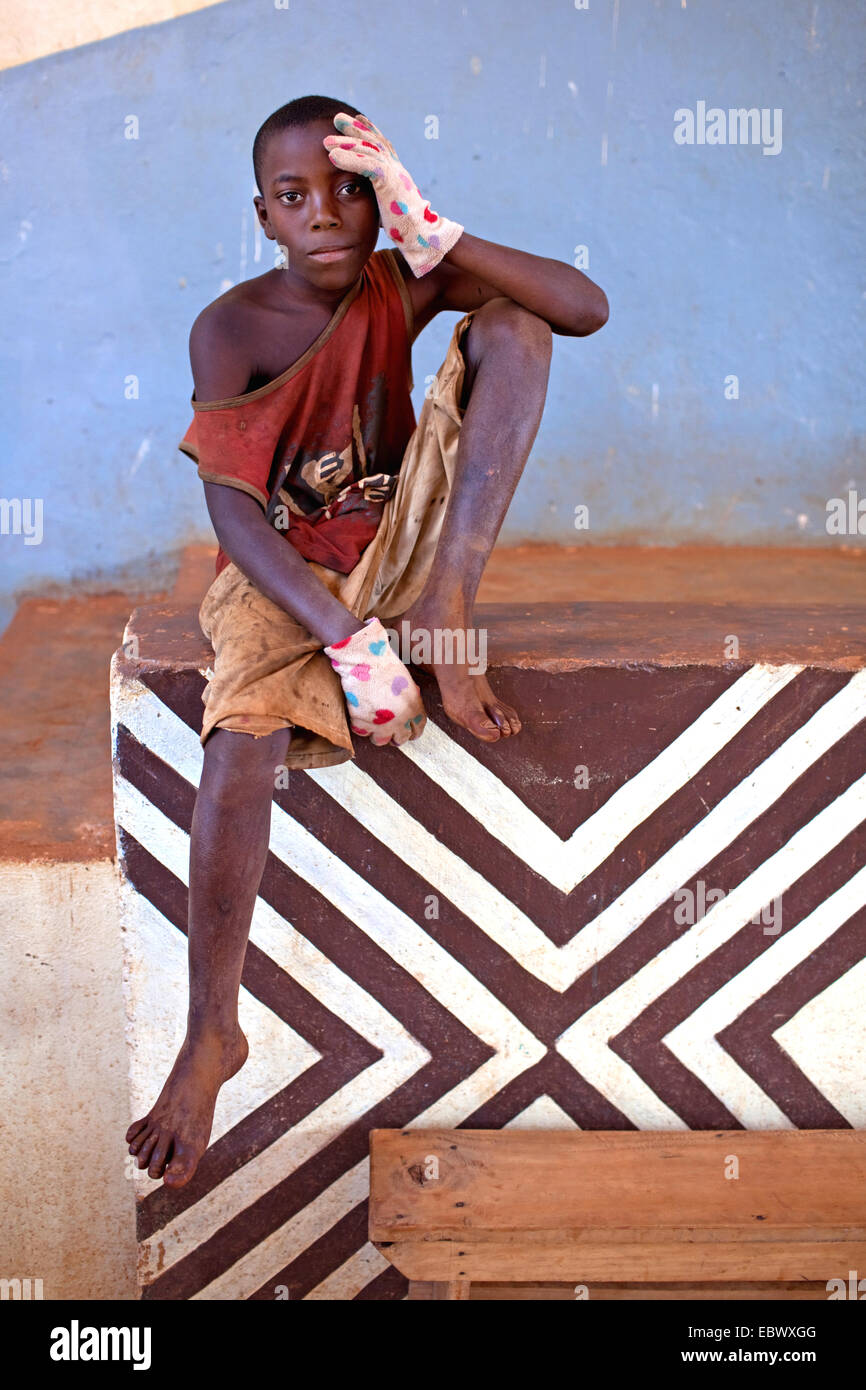 Junge in schäbigen Kleidung sitzt auf Wand, Burundi, Karuzi, Buhiga Stockfoto