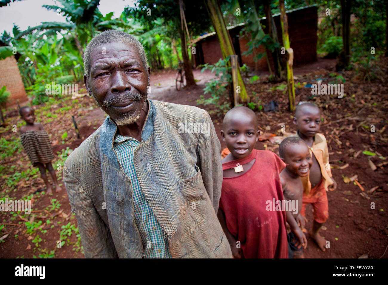 Großvater mit einem zerrissenen Mantel steht mit seinem Enkel vor seinem einfachen Lehmhaus, Uganda, Jinja Stockfoto