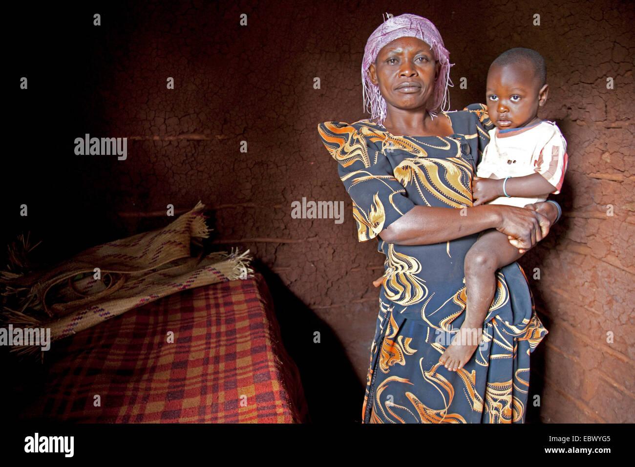 Mutter steht mit ihrem Sohn auf dem Arm in einfache Schlafzimmer ein Lehmhaus, Uganda, Jinja Stockfoto