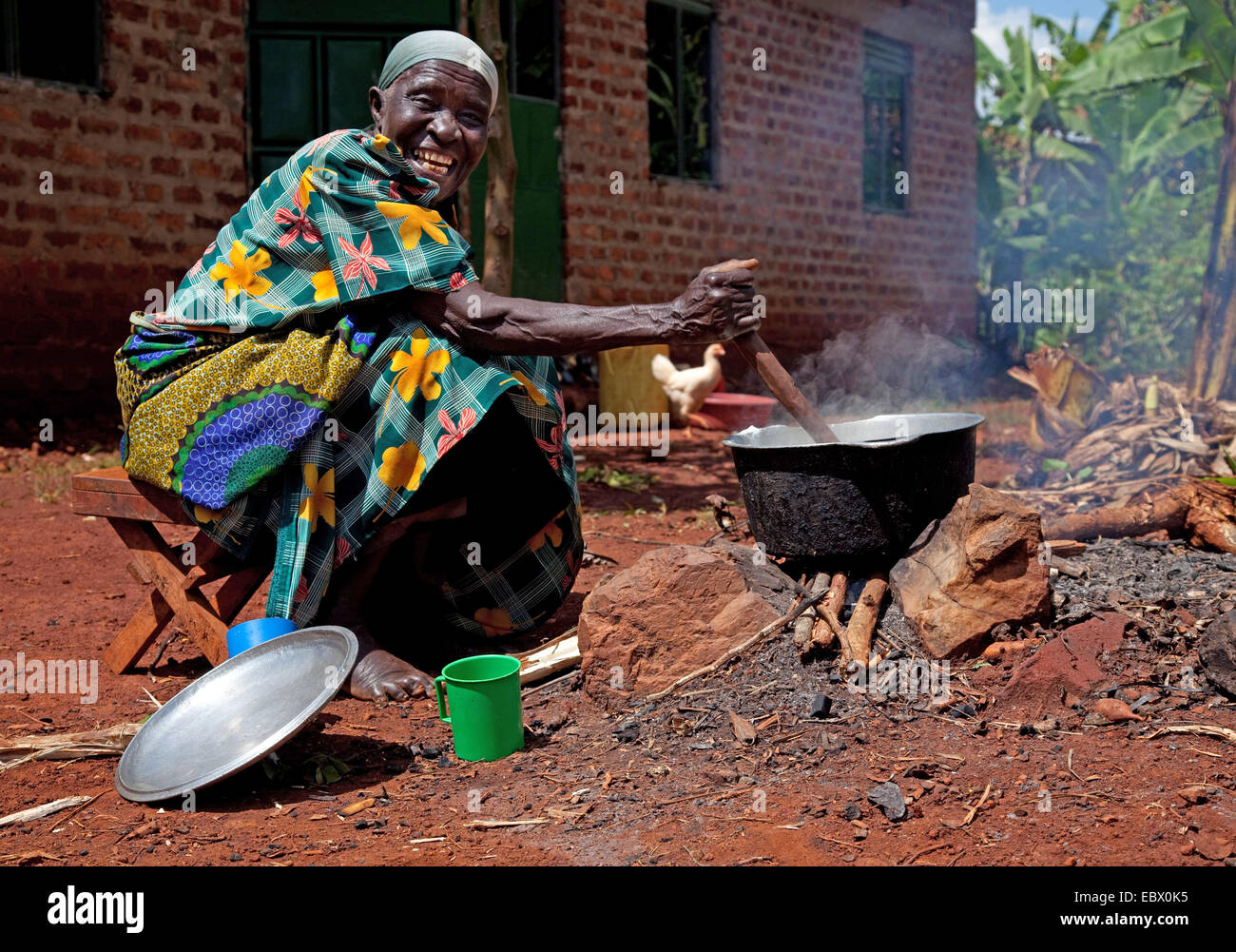 glückliche alte Frau kocht Reis auf einen offenen Kamin vor ihrem Haus, Uganda, Jinja Stockfoto