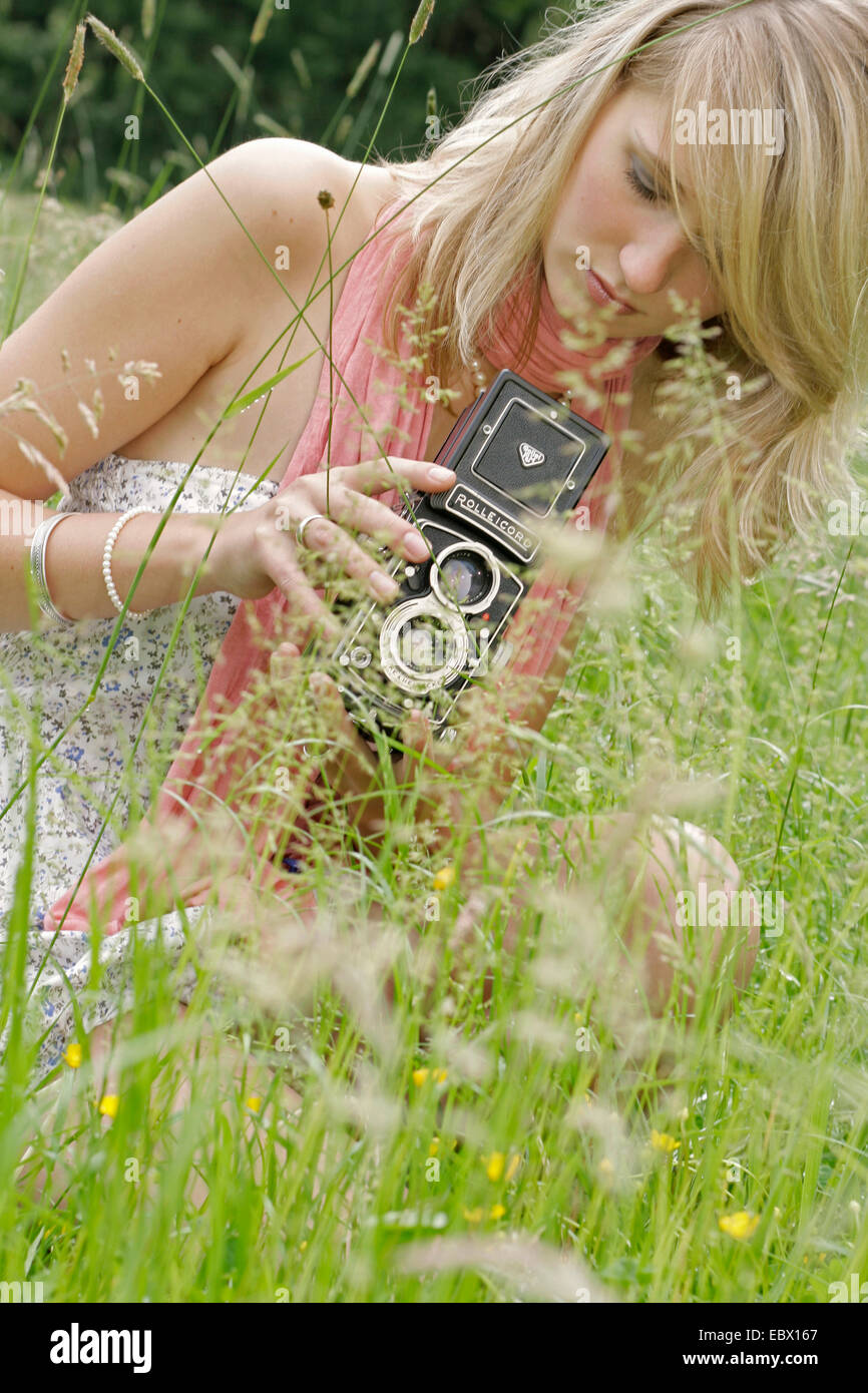 attraktive junge Frau sitzt mit alten Foto-Kamera auf einer Wiese, Deutschland Stockfoto