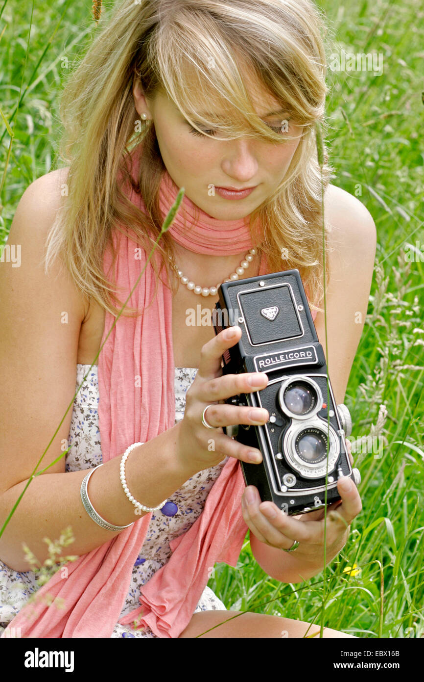 attraktive junge Frau mit alten Foto-Kamera sitzt auf einer Wiese, Deutschland Stockfoto
