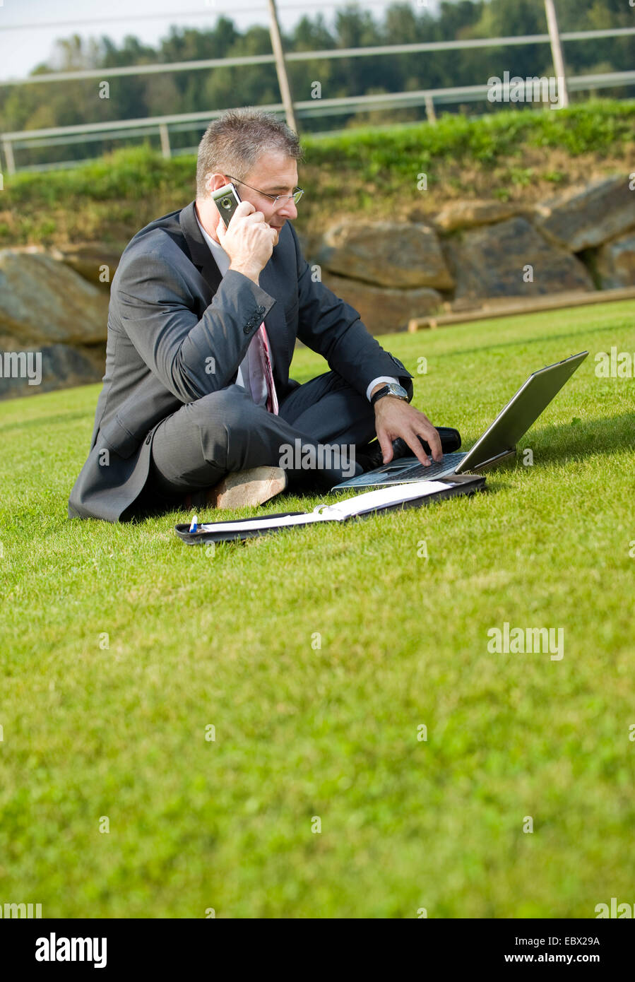Geschäftsmann, sitzen auf einer Wiese mit Laptop und Handy Stockfoto